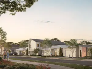 A suburban street at dusk features modern houses, well-kept gardens, parked cars, and people walking and cycling along the sidewalk under a clear sky.